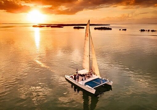 The Carolina Moon catamaran sailing across glassy golden water of Florida Bay at sunset in Key Largo