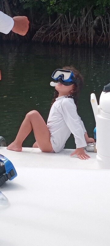 A young girl wearing a snorkel mask sitting on the deck of a boat on a Key Largo family snorkeling trip