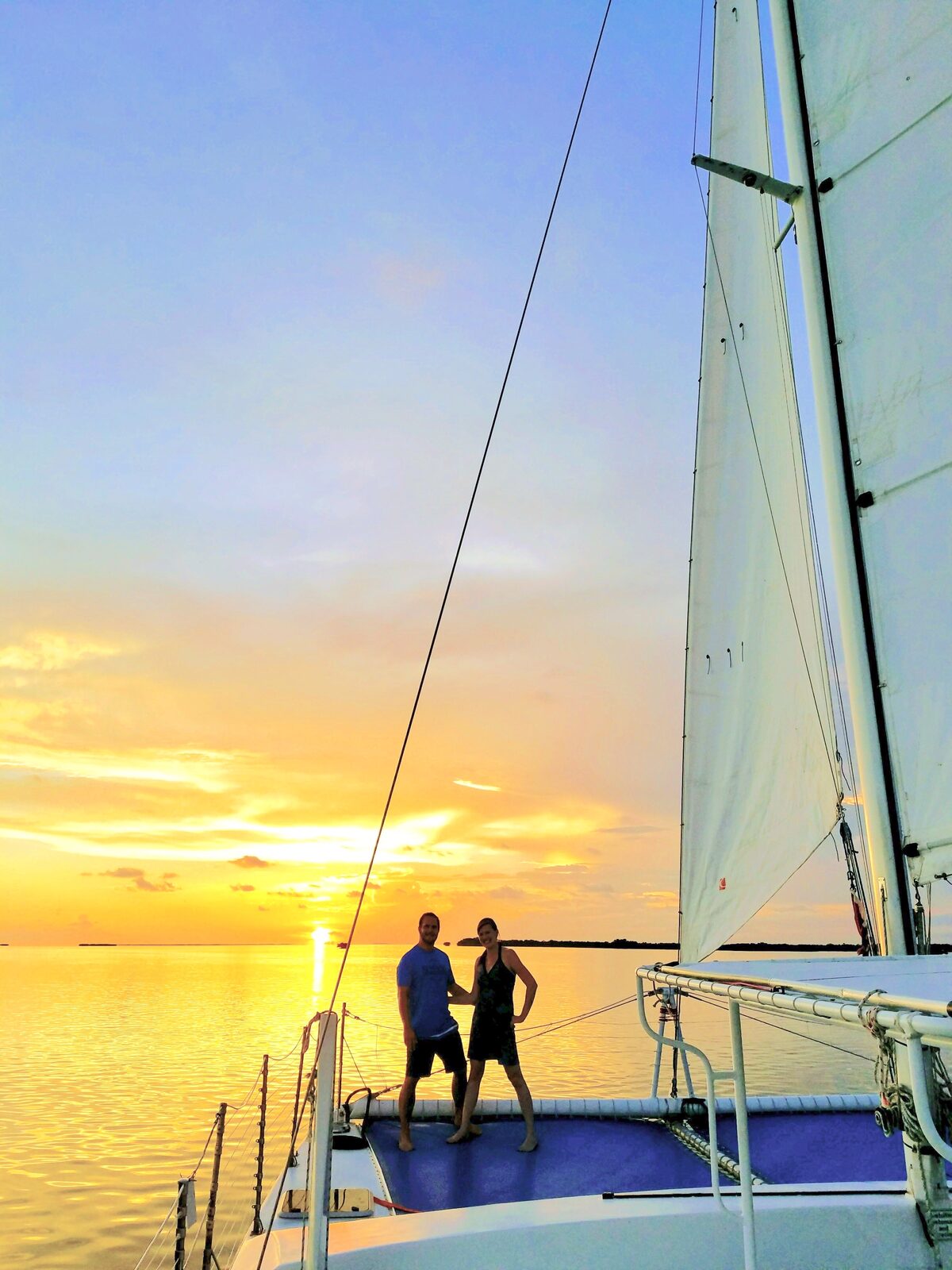 A couple standing on the bow of a catamaran watching a brilliant golden sunset over Florida Bay in Key Largo