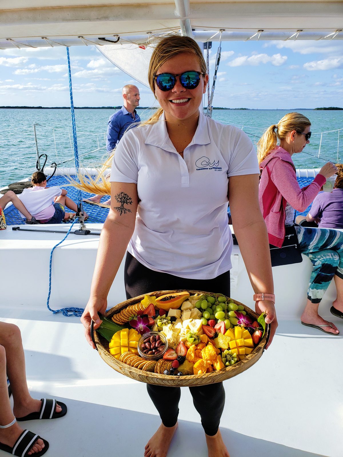 A smiling Caribbean Watersports crew member presenting a fresh fruit platter aboard the Carolina Moon