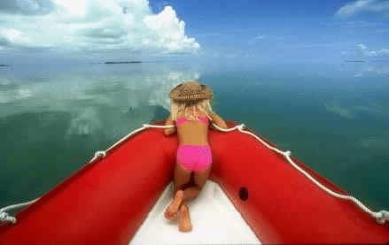 A young girl in a straw hat kneeling on the red bow of the original Enviro-Tours boat over mirror-calm Florida Bay