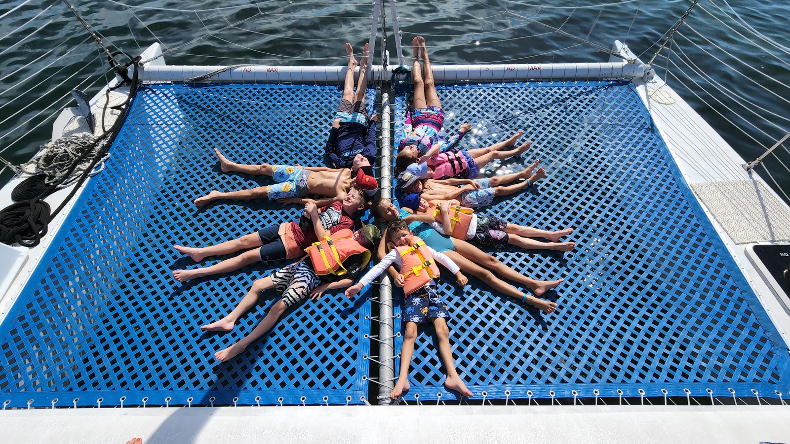 Friends lying in a star formation on the trampoline of the Carolina Moon catamaran over blue Florida Bay water