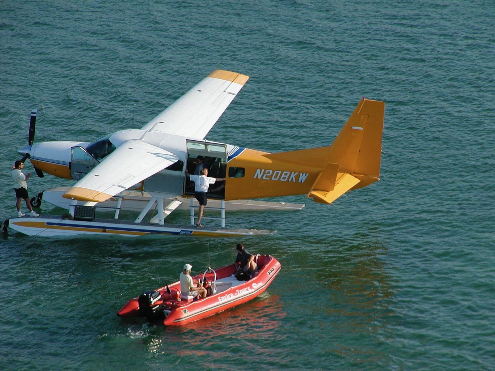 A yellow and white seaplane floating beside the red Enviro-Tours boat on clear shallow water