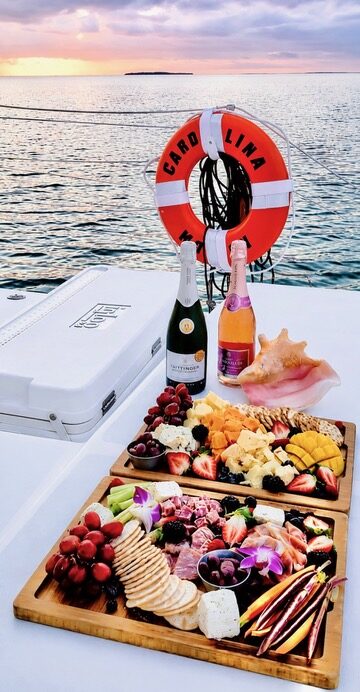 Champagne bottles, a conch shell and a charcuterie and fruit spread set out at sunset aboard the Carolina Moon catamaran in Key Largo
