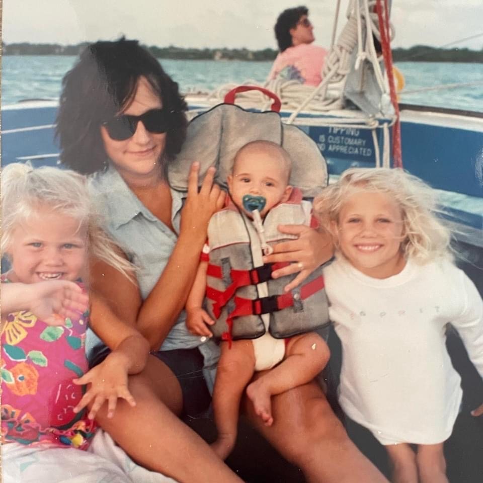 A mother holding a baby with two young girls aboard a sailboat in a vintage family photo