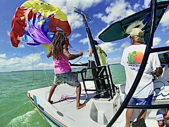 Crew members guiding a colorful parasail back onto the deck of the chase boat