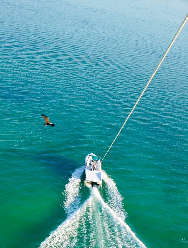 Looking down the towline from a parasail at the boat far below on turquoise water