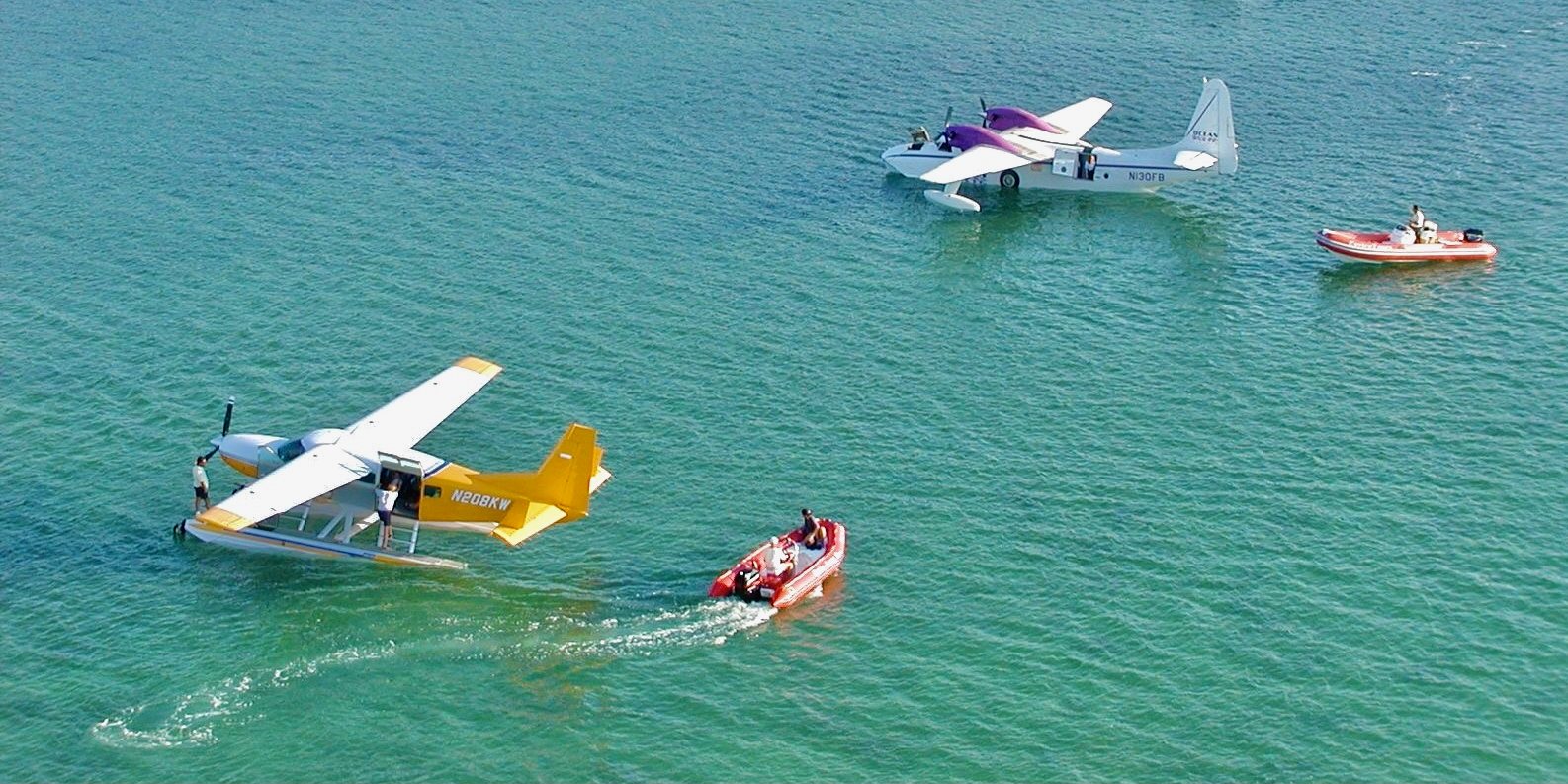 A seaplane floating on shallow turquoise water beside the red Enviro-Tours boat in the backcountry