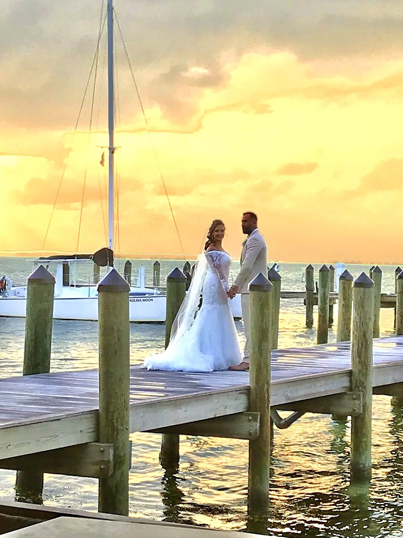 Bride and groom on a Key Largo dock at sunset beside the Carolina Moon catamaran